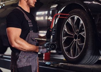 Muscular man is fixing car's wheel with special tool at auto service.